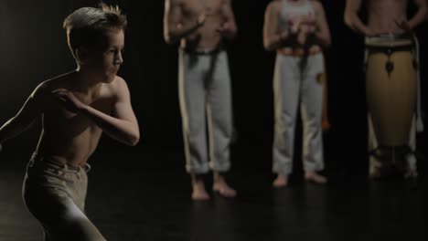 un grupo de bailarines profesionales están practicando capoeira en la oscuridad contra un foco de luz en un fondo negro de estudio. arte marcial afro-brasileño que combina elementos de la danza.