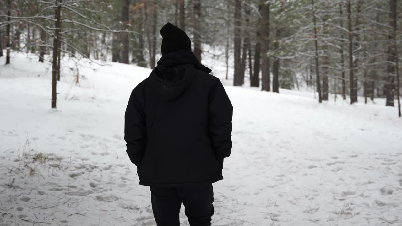 hombre vestido de negro caminando por un bosque blanco de invierno cubierto de nieve
