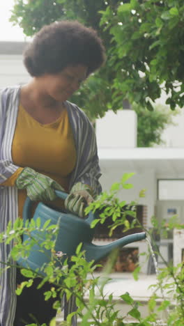 video de una feliz mujer afroamericana de tamaño grande regando flores en el jardín