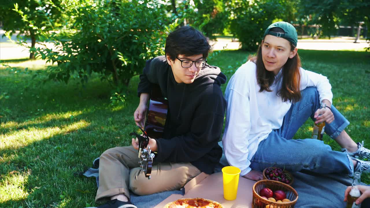 친구 들 이 공원 에서 피크닉 을 즐기고 기타 를 연주 하고 있다