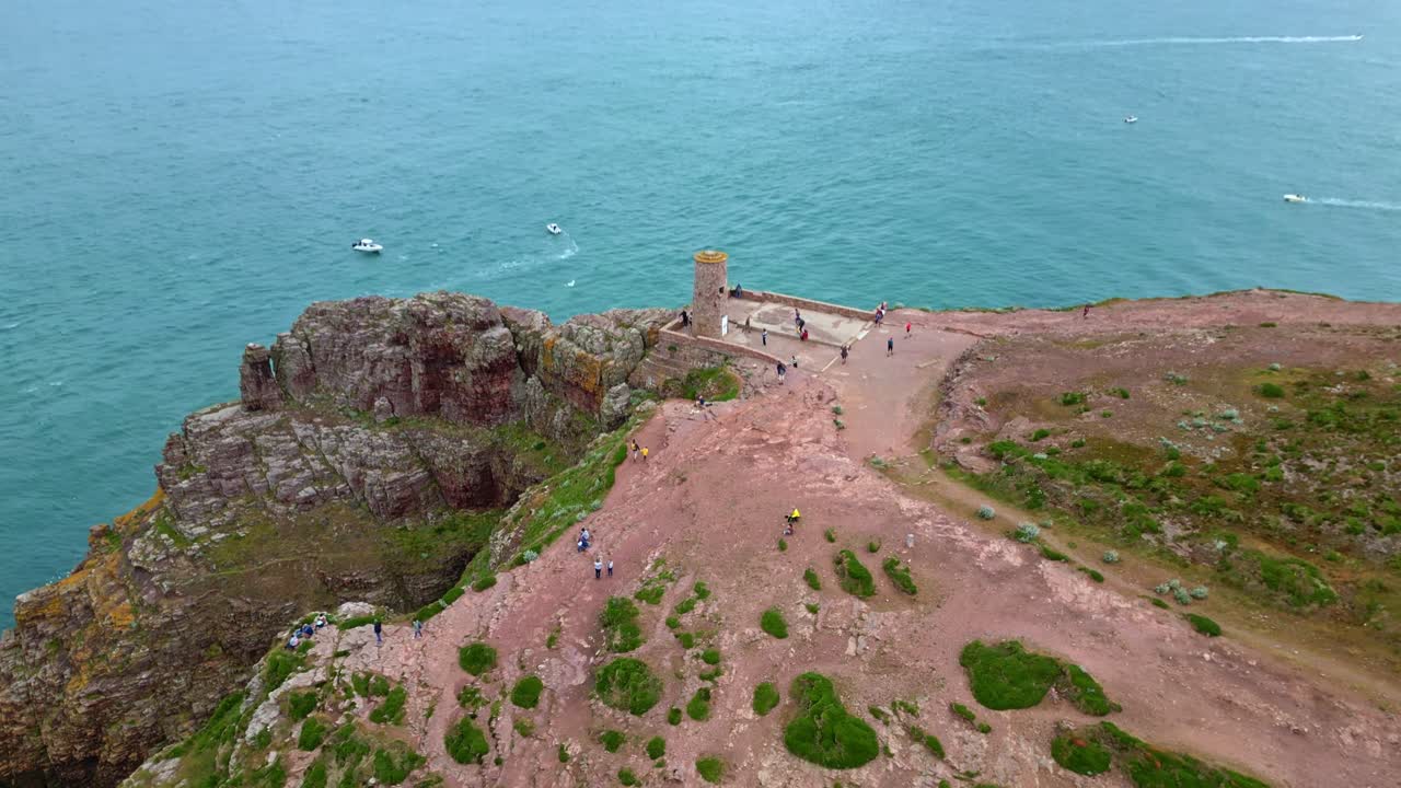 Historic stone tower on rugged cliffs of Cap Fréhel, people and sea, Brittany, France. Aerial drone pov