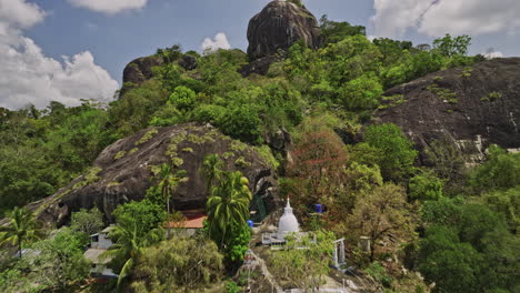 Algama-Len-Viharaya-Sri-Lanka-Antena-V4-Paso-Elevado-Bajo-Antiguo-Templo-Budista-Ubicado-En-La-Ladera-Hacia-La-Cima-De-La-Montaña-Rocosa-Que-Captura-El-Entorno-De-Los-Arbustos-De-La-Jungla---Filmado-Con-Cine-Mavic-3---Abril-De-2023