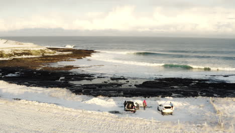 Aerial-dolly-at-sunrise-as-surfers-gather-around-cars-looking-out-over-pristine-winter-waves-on-cold-day