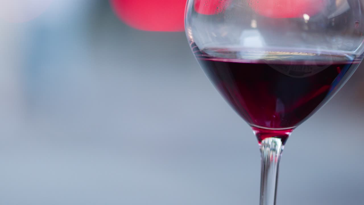 Primo piano di vino rosso versato in un bicchiere, luci bokeh, atmosfera serale soffusa all'aperto