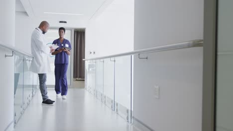 afrikanisch-amerikanische männliche und weibliche ärzte mit schreibtafel und tablet sprechen im krankenhaus