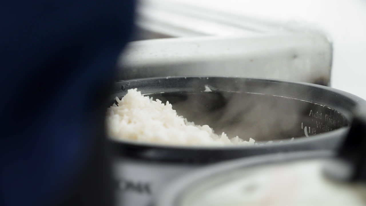 Perfectly cooked fluffy white rice scooped out onto plate from steaming rice cooker, slow motion close up 4K