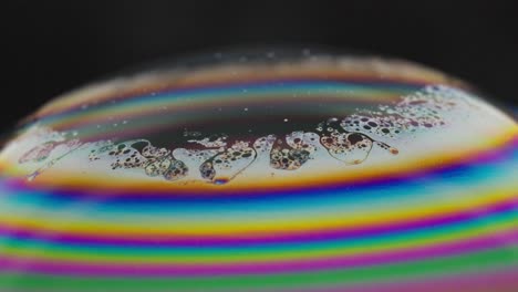 close-up of a rainbow-colored soap bubble with intricate patterns against a dark background