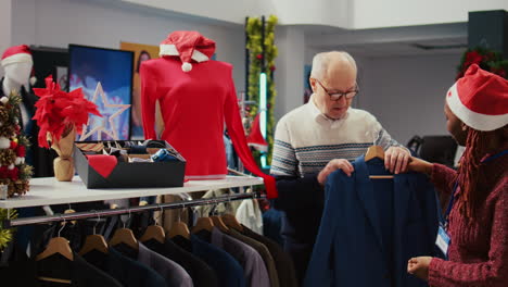 empleado hábil en una tienda de ropa decorada navideña vendiendo una chaqueta lujosa a un cliente senior rico, convenciéndolo de que la prenda está magistralmente elaborada con materiales de calidad.