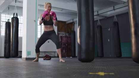 una boxeadora caucásica con guantes de boxeo pateando el saco de boxes en el gimnasio