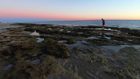 a man with an orange frisbee navigates across the tide pools left after the tide has gone out, puerto peñasco, gulf of california, mexico