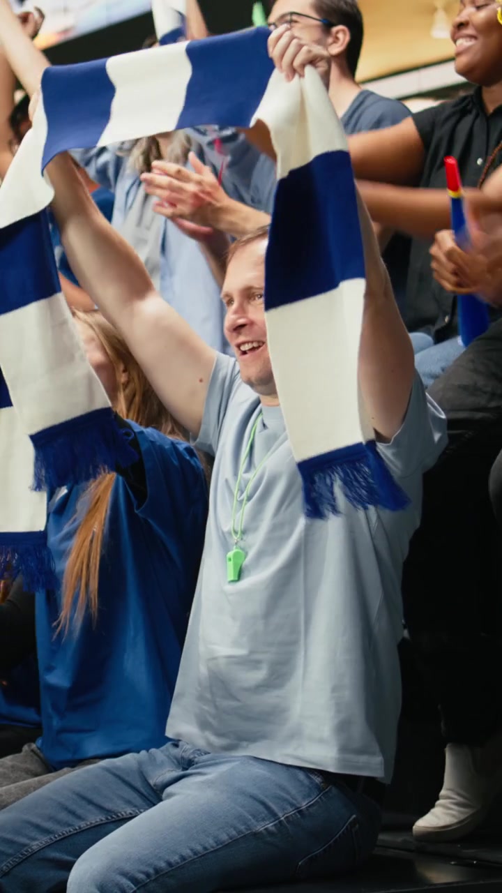 Vertikal video: Begeistrede fotballsupportere fra det blå laget hever armene og jubler på stadion.