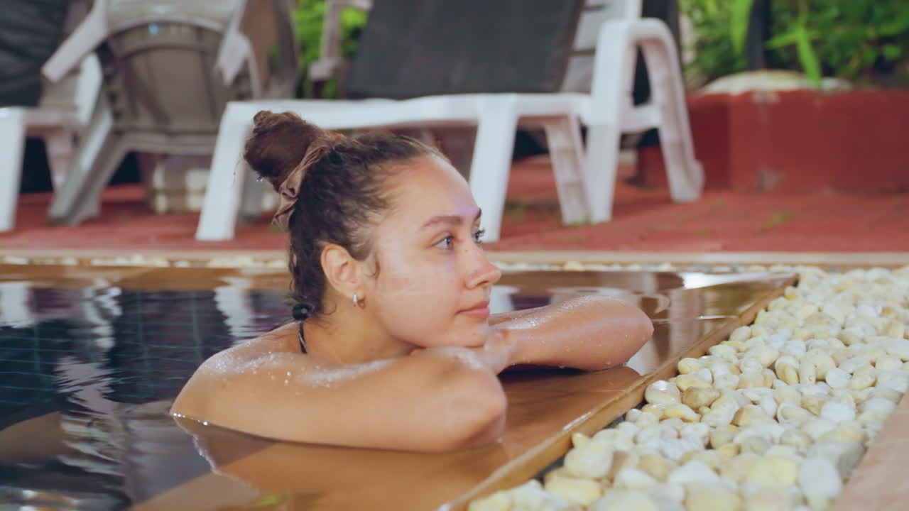 Scena di riposo tropicale. Donna dell'isola che si rilassa a bordo piscina. Serena donna polinesiana che riposa su un bordo piscina in legno. Calma donna dell'isola che si gode il tempo libero tra luci calde e un'atmosfera da spa.