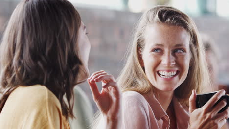 two young female friends meeting sitting at table in coffee shop and talking