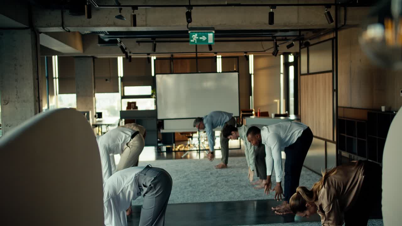 Overview of a group of business people in business attire doing yoga during a break at work in the office. Taking care of