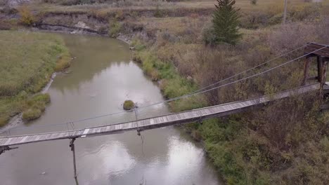 battered and neglected old suspension bridge over tiny badlands river