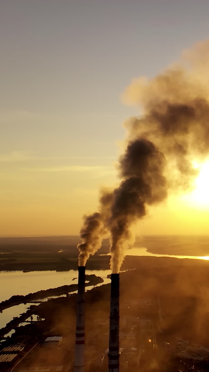 Industrial pipes with thick smoke at sunset. Two large pipes produce chemical smoke in the air on nature background. Environmental pollution. Vertical video