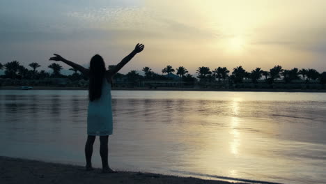 Young-woman-in-staying-at-beach.-Beautiful-girl-raising-hands-at-seaside.