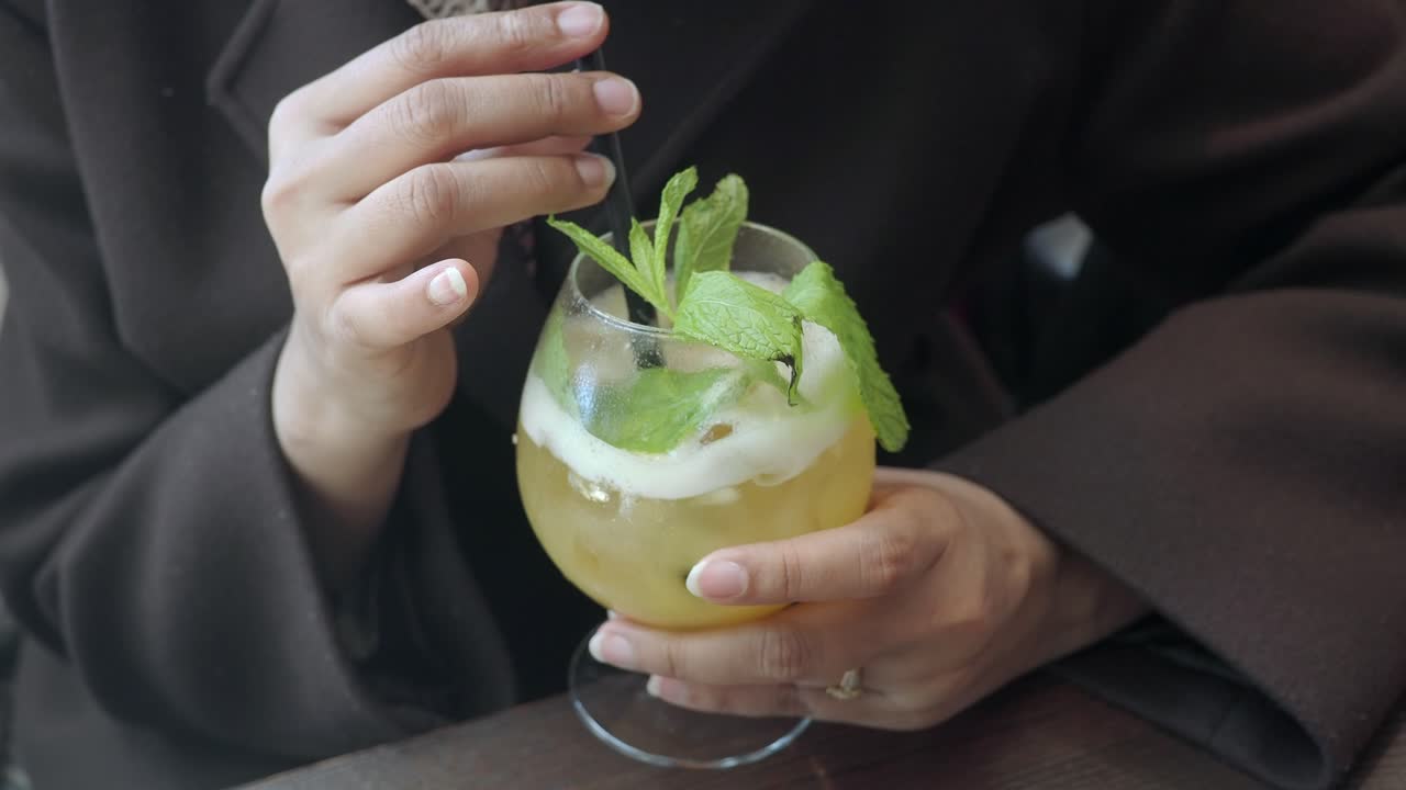 Nærbilde av hender som rører en forfriskende cocktail med mynte