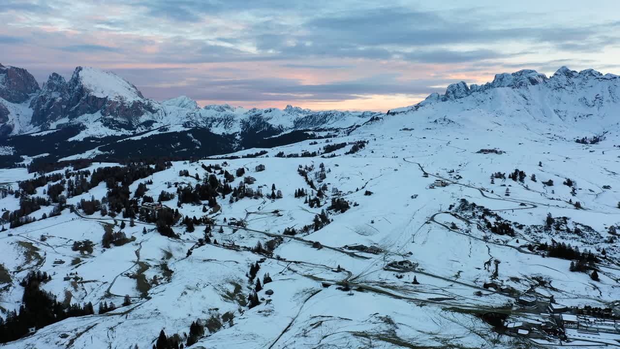 Ripresa aerea panoramica del prato alpino innevato dell'Alpe di Siusi (Seiser Alm) e della catena montuosa delle Dolomiti in Alto Adige, Italia al tramonto