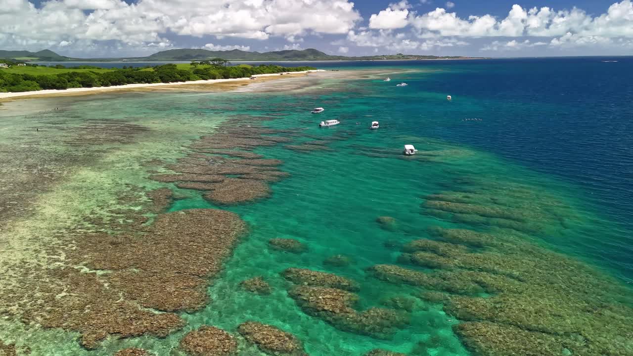An aerial shot showcasing boats floating over a sprawling coral reef, with clear turquoise water revealing the vibrant marine ecosystem below