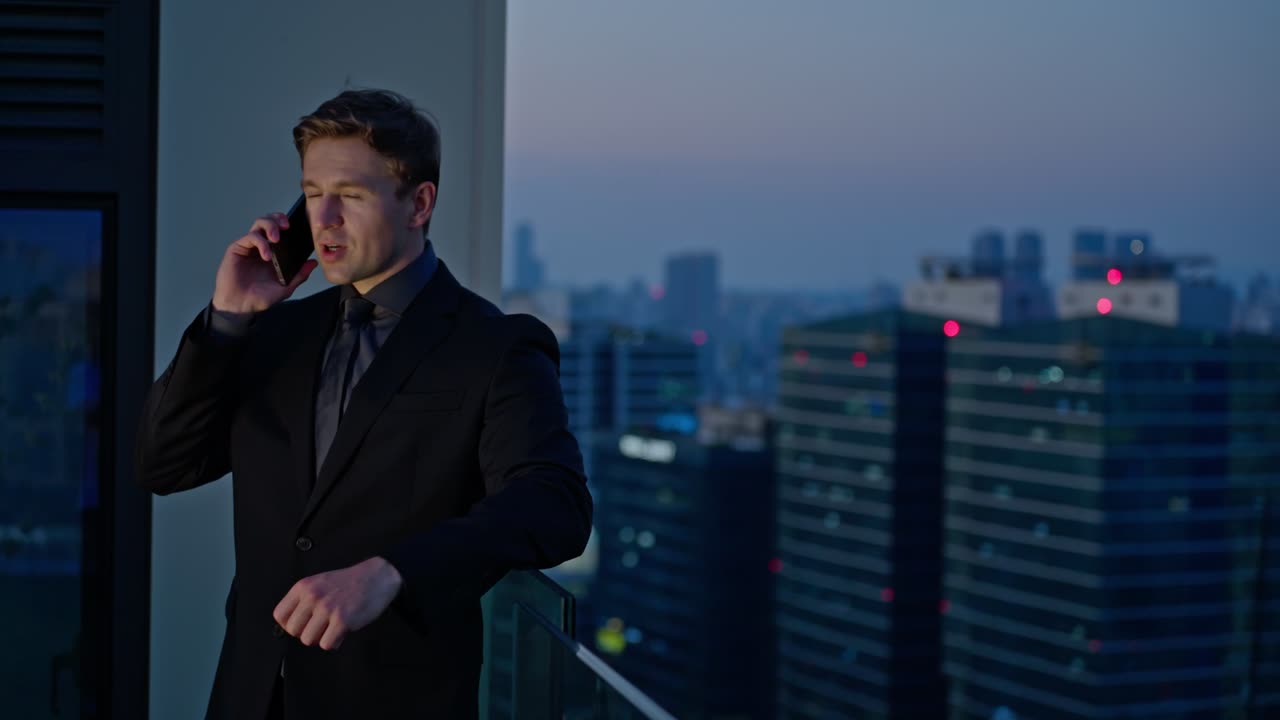 A serious-looking businessman in a dark suit takes an important phone call on a rooftop with a city skyline at dusk, symbolizing high-stakes decision-making
