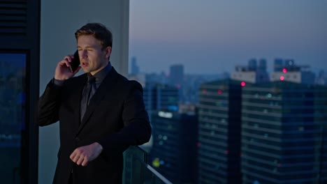 a serious-looking businessman in a dark suit takes an important phone call on a rooftop with a city skyline at dusk, symbolizing high-stakes decision-making