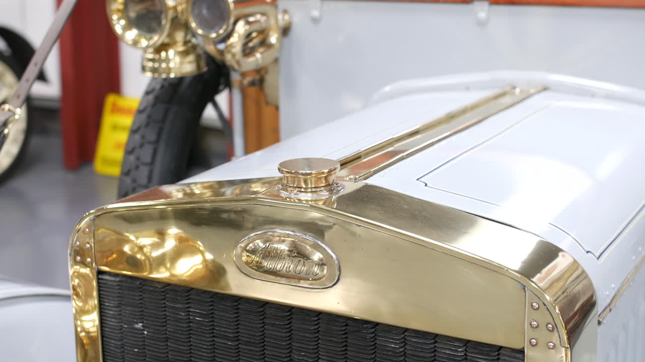 A car with a polished brass grille and Albion badge is presenting vintage detailing on a white hood, featuring a central cap and finely ribbed metalwork
