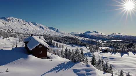 snow covered wooden chalets are nestled in a serene valley, surrounded by snow capped mountains and a clear blue sky, creating a picturesque winter landscape during a bright sunny day