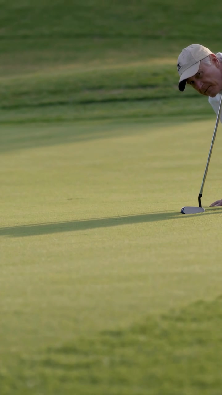 Video verticale: Golfista che si prepara per un putt sul green, regolando palla e putter, con cappellino, spazio per il testo.