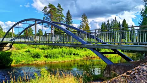 Metal Arch Bridge Crossing River Surrounded by Greenery and Trees in Summer