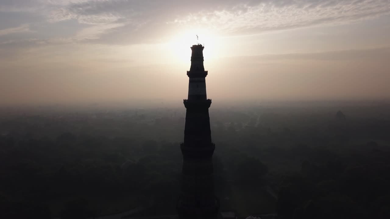 Tháp Qutub Minar đứng sừng sững với bóng đổ và ánh sáng chói của máy ảnh trước bầu trời bình minh mờ ảo ở New Delhi, Ấn Độ. Khói bụi dày đặc và ô nhiễm không khí che khuất cảnh quan thành phố xung quanh di tích lịch sử.