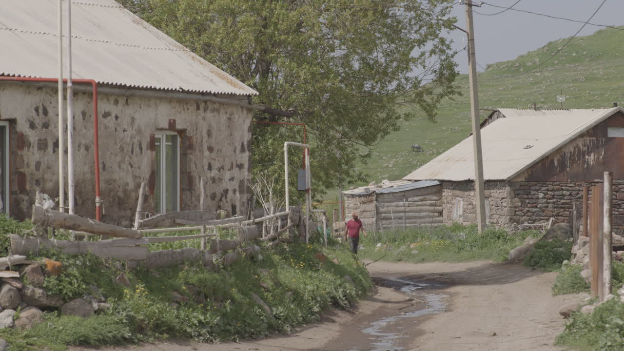 조지아의 타바츠쿠리 호수 옆 몰리티의 작은 마을에서 전통 가옥이 보이는 흙길을 걷는 남자