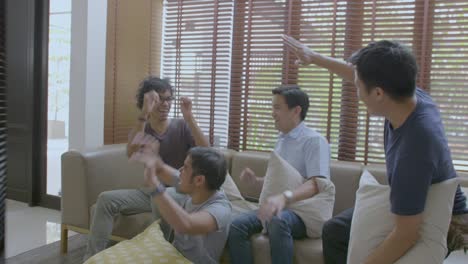 group of asian flat mates watching sports competition on tv at home