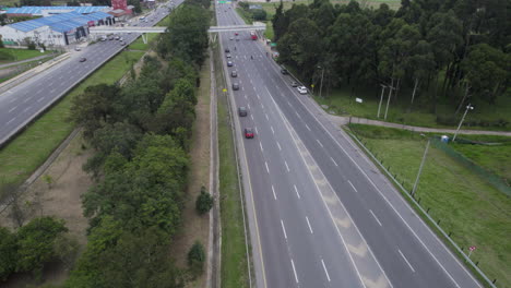 Overhead-Drohnenclip-Einer-Großen-Autobahn-Mit-Schnell-Fließendem-Verkehr-In-Beide-Richtungen,-Mit-Gebäuden,-Bäumen-Und-Gras-An-Den-Seiten