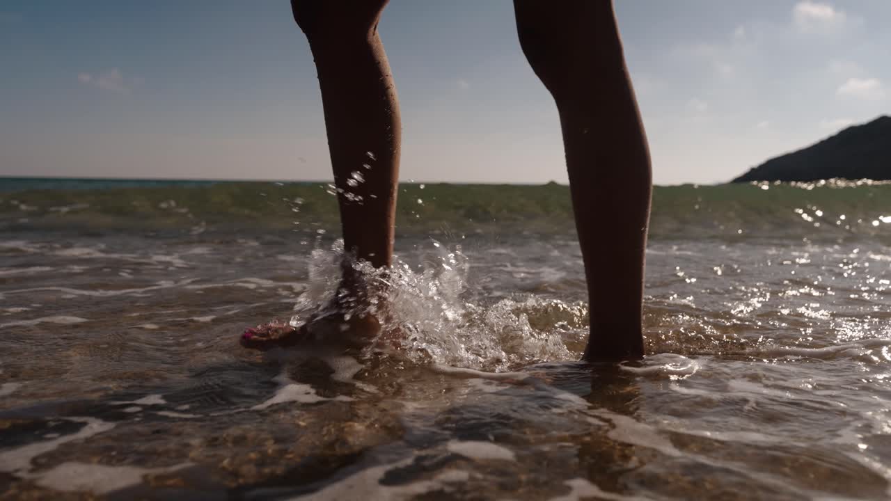 Bare feet splash gently through foamy waves on the shoreline in this dynamic slow-motion beach scene in Algarve