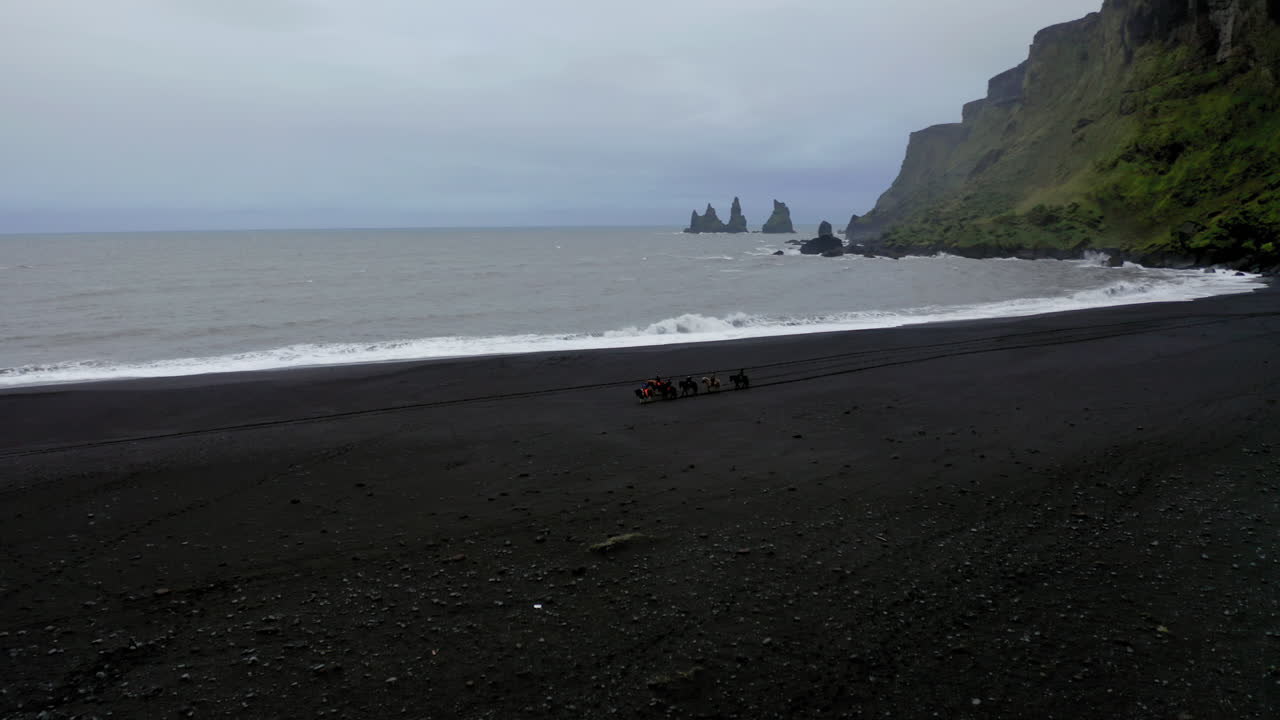 antena: toma panorámica lenta de un grupo de turistas montando caballos en la playa de vik en islandia