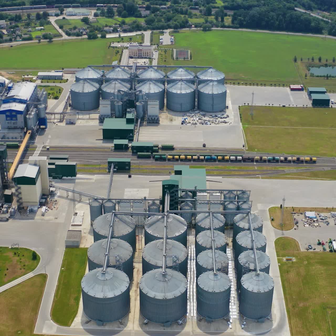 New industrial complex with grain silos. Grain storage tanks in the countryside. Modern grain-drying farm with large silver terminals in rural landscape. View from above