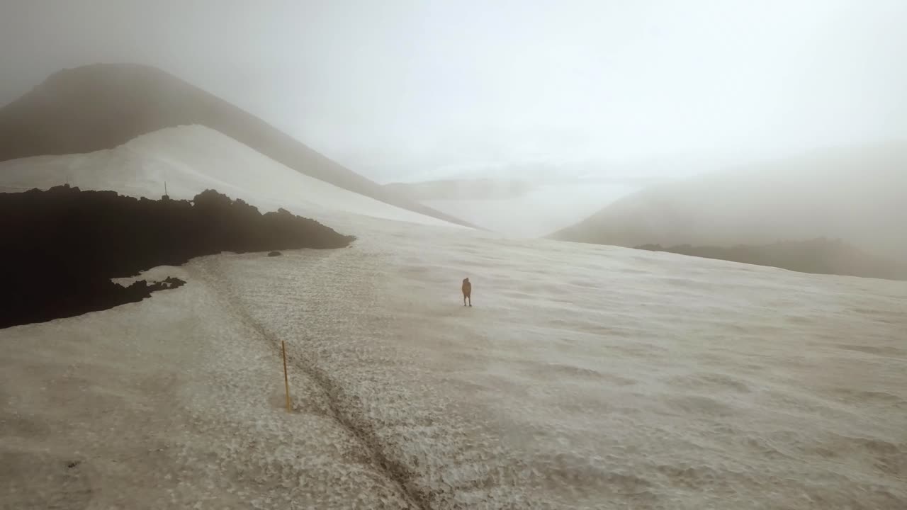 Aerial landscape view of a person hiking on a snow capped mountain, on a foggy day, Fimmvörðuháls area, Iceland
