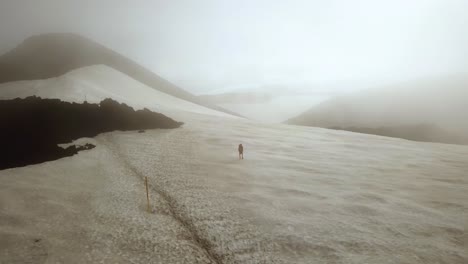 Aerial-landscape-view-of-a-person-hiking-on-a-snow-capped-mountain,-on-a-foggy-day,-Fimmvörðuháls-area,-Iceland