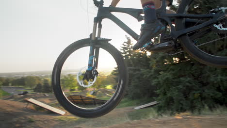 Man-on-mountain-bike-launches-up-a-dirt-ramp-and-kicks-back-tire-towards-the-camera