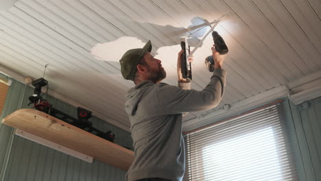 man uses cordless drill to fasten mounting bracket for camera to ceiling