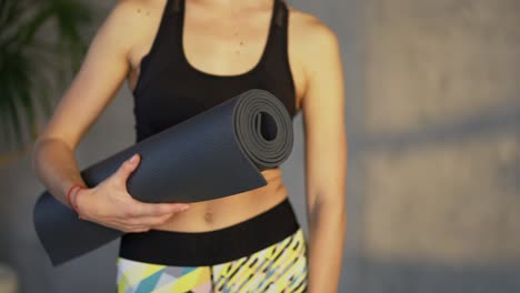 Close-up-overview-of-a-woman-athlete-posing-with-mat-in-hand-standing-in-loft-room