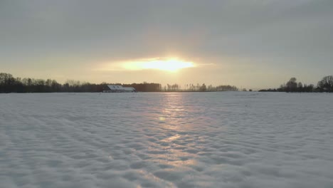 Low-angle-aerial-view-of-snowy-white-field-at-sunset,-northern-Europe,-forward