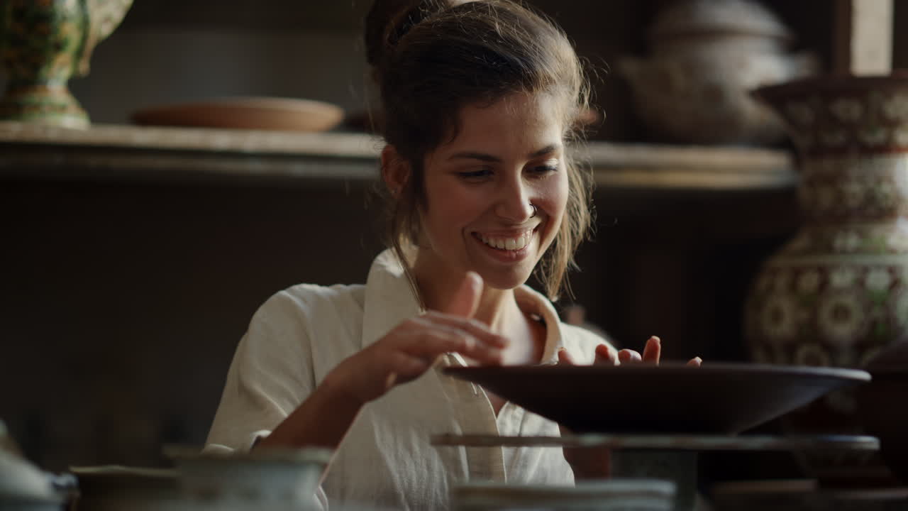 유쾌 한 예술가 가 스튜디오 에서 도자기 바 ⁇  를 가지고 놀고 있다. 여자 가 점토 접시 를 즐기고 있다