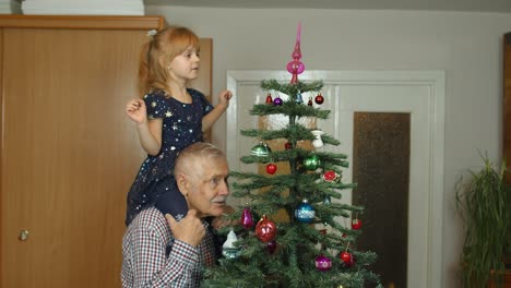 Niña-Con-Abuelo-Mayor-Decorando-árbol-De-Navidad-Artificial-Con-Adornos-Juguetes-En-Casa