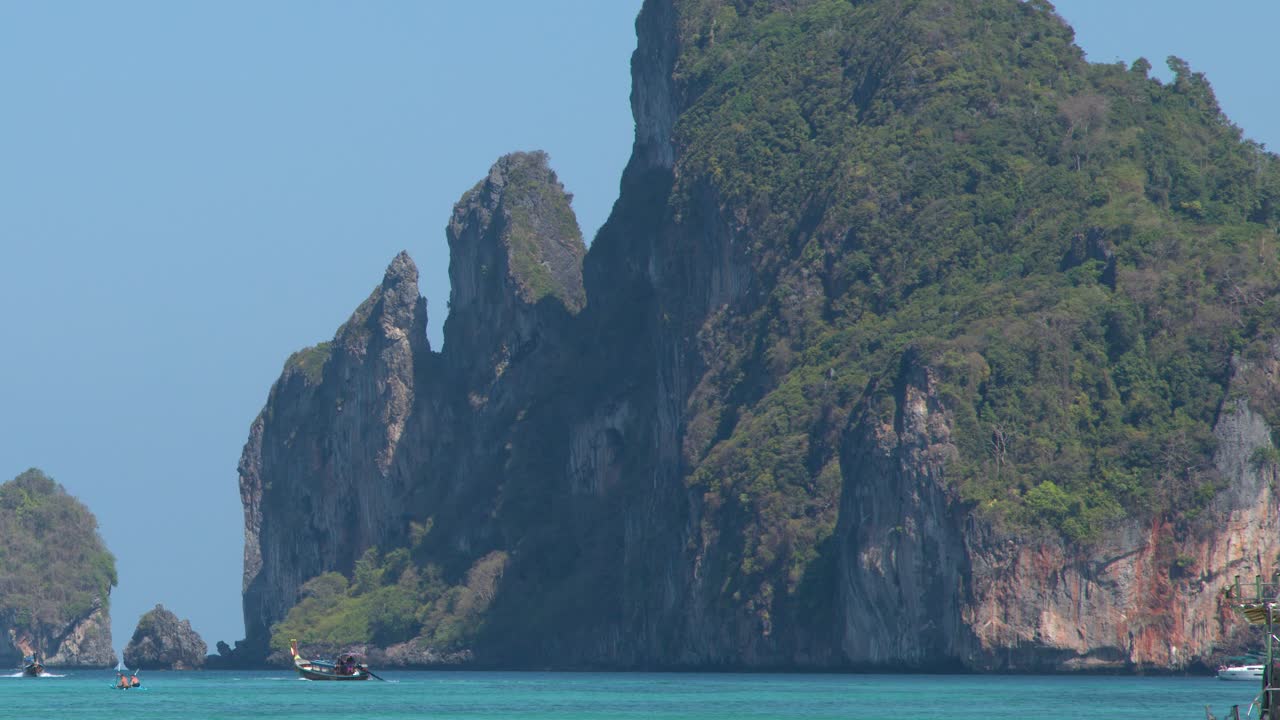 Một chiếc thuyền đuôi dài truyền thống lướt trên mặt nước màu ngọc lam ngang qua những vách đá vôi cao chót vót dưới bầu trời trong xanh.