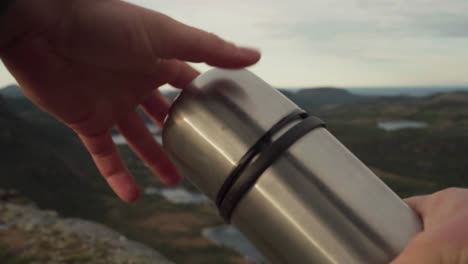 persona abriendo un frasco térmico de café durante una caminata por la montaña