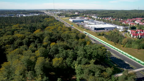 Aerial---flying-a-drone-over-the-trees-near-the-expressway---urban-agglomeration-with-industrial-warehouses-and-residential-buildings-in-the-background