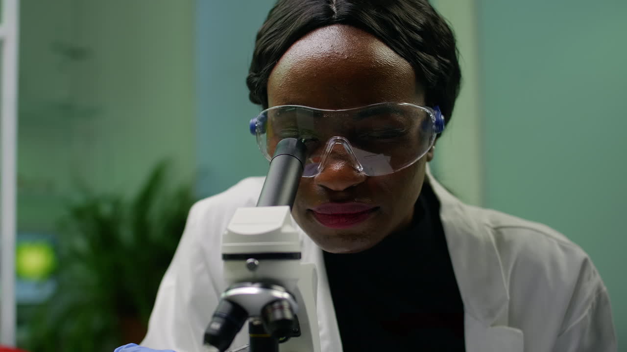 Closeup of african researcher woman looking at leaf slide under microscope
