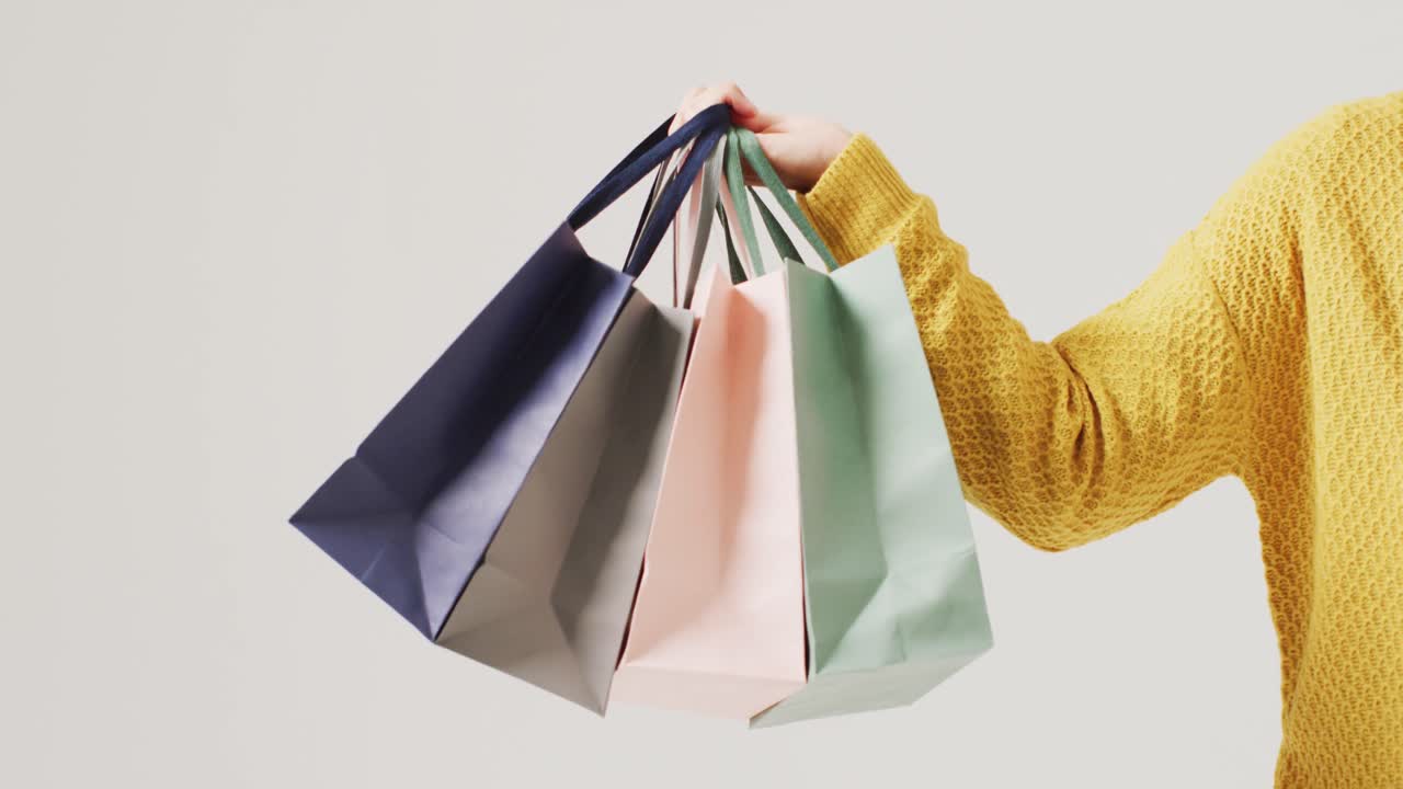 brazo de una mujer sosteniendo bolsas de regalos de colores sobre fondo blanco
